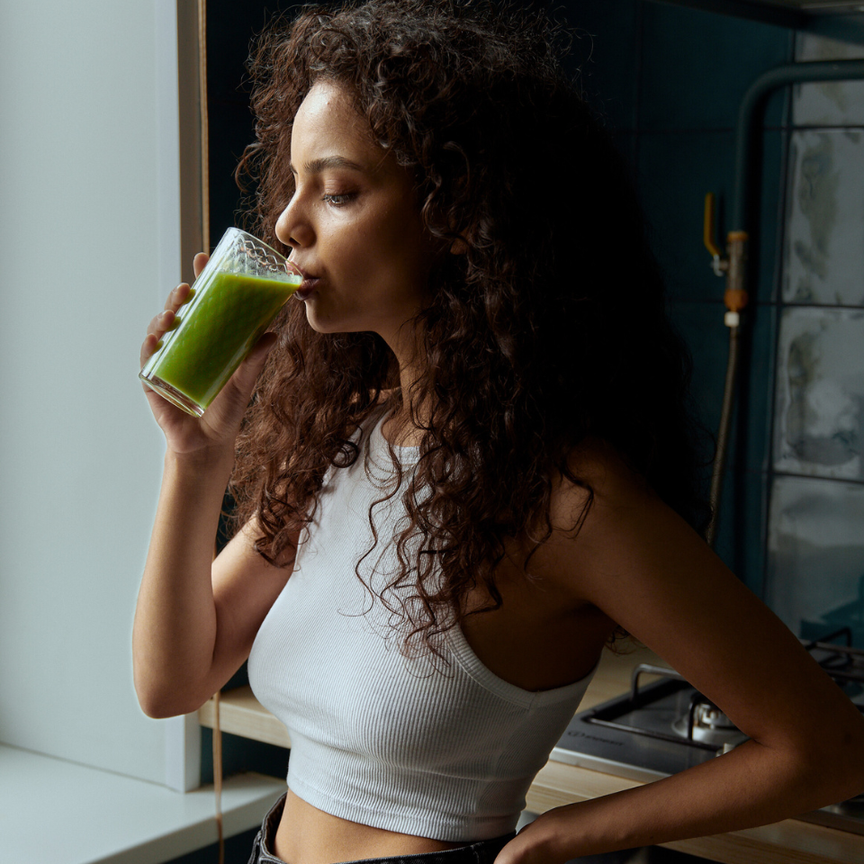 Woman drinking a green smoothie in a kitchen.