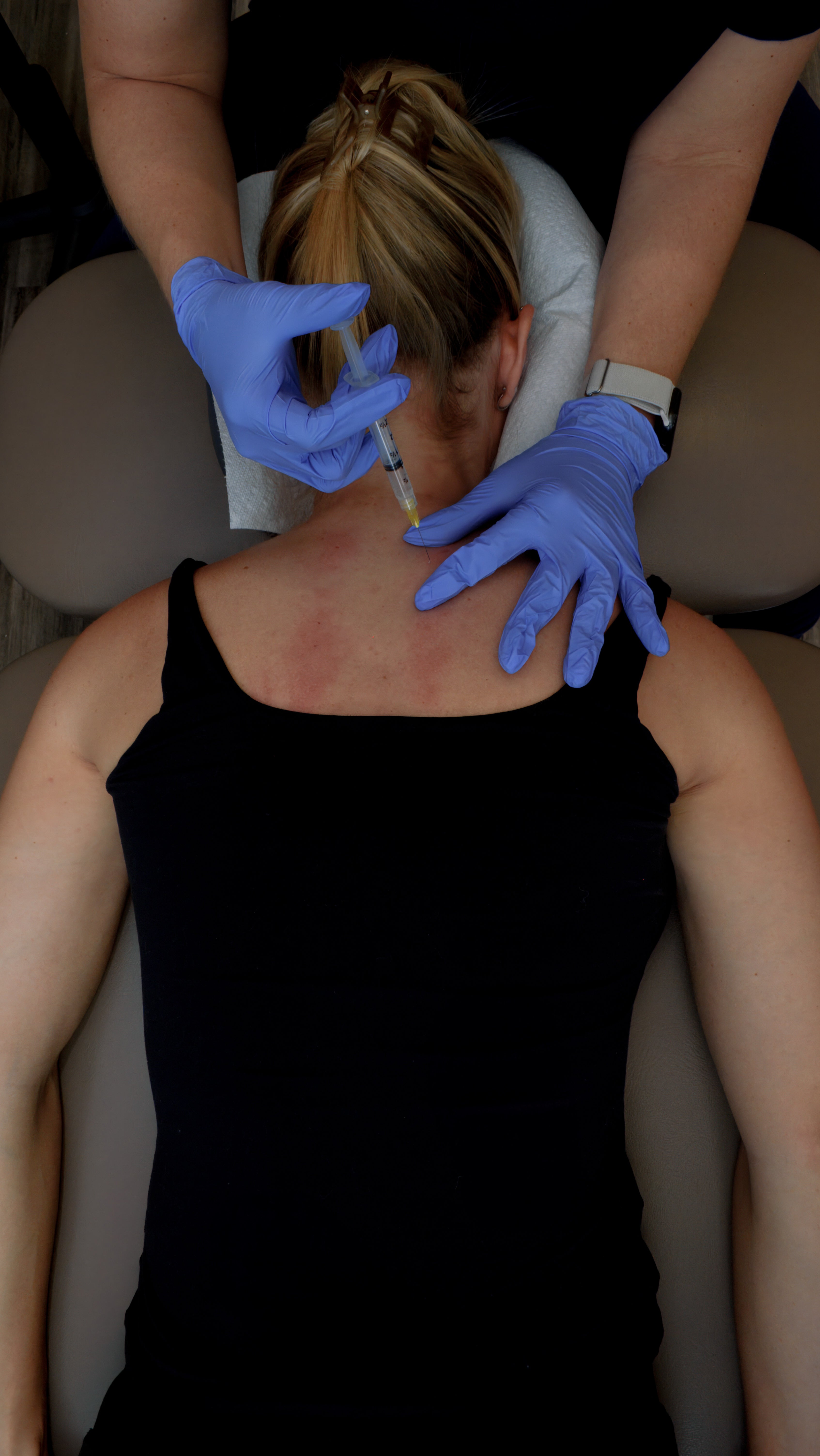 Person receiving an injection on the neck from another person wearing blue gloves.