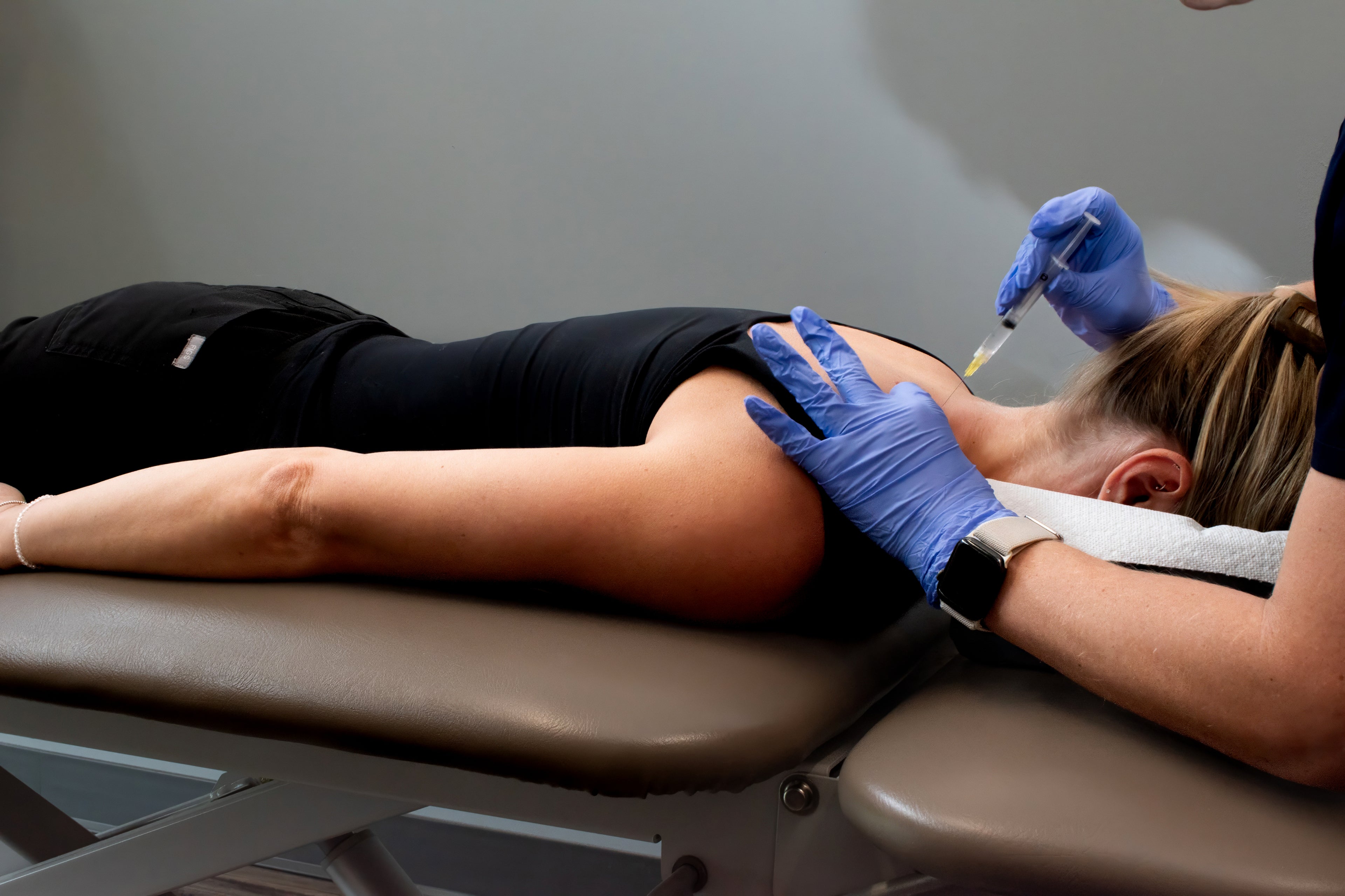 Person receiving an injection on a medical table with a neutral background