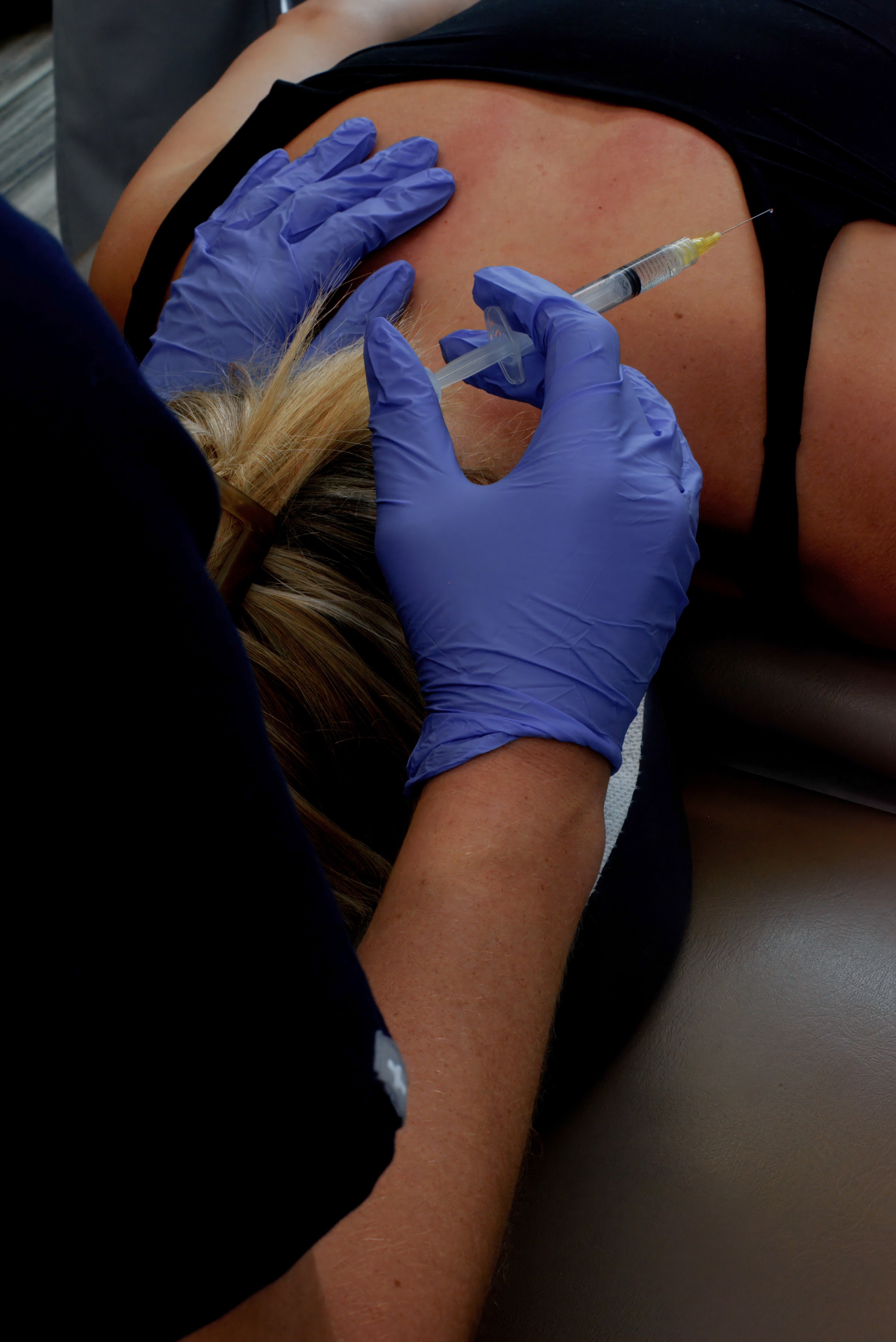 Person receiving an injection on the back with gloved hands