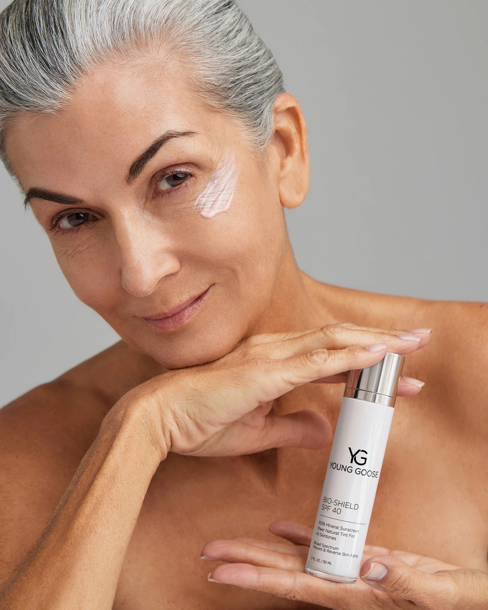 Woman applying skincare product with a bottle labeled 'YG' on a gray background