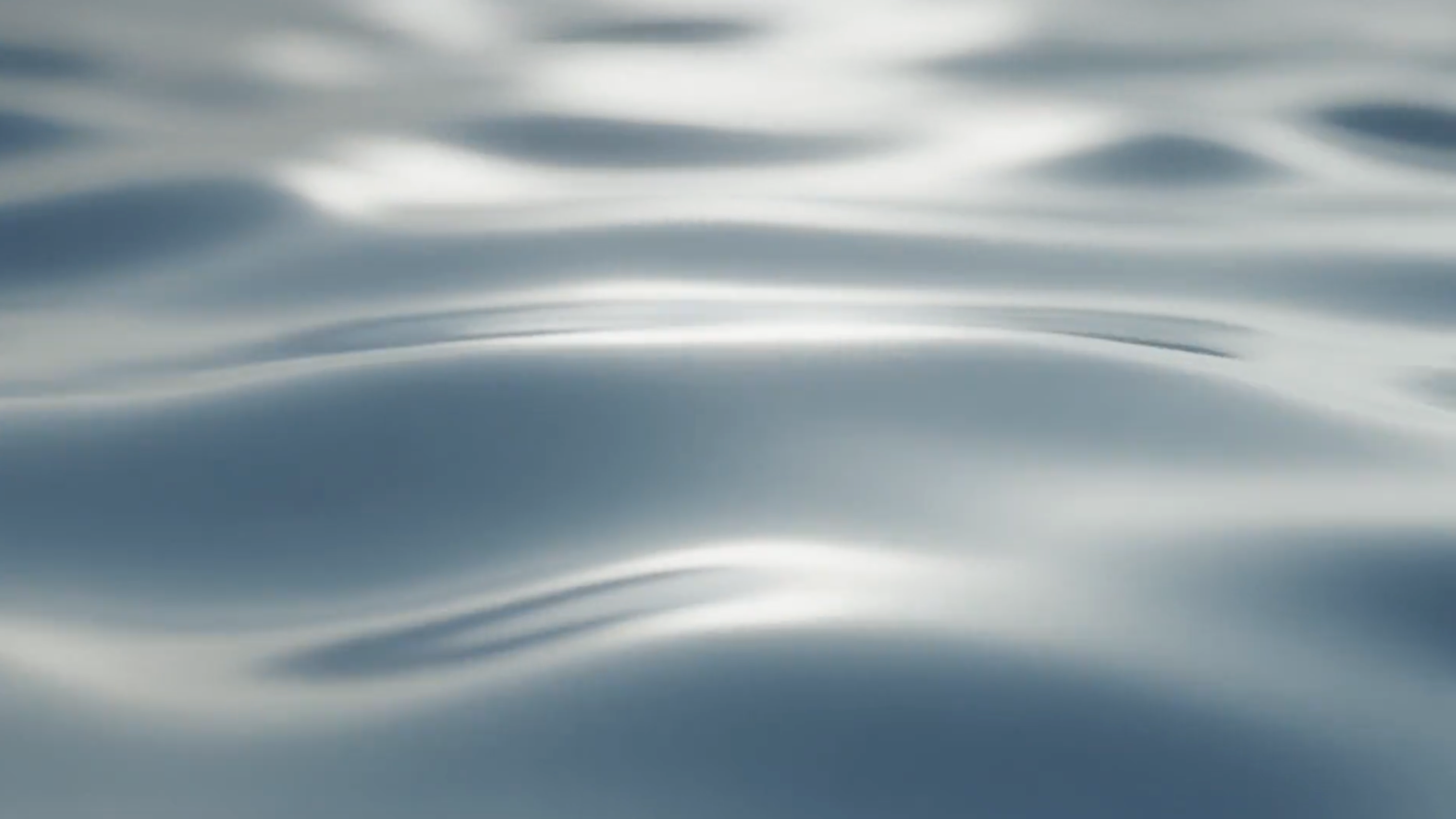 A close-up abstract view of rippling water with soft blue-gray tones and bright white highlights.