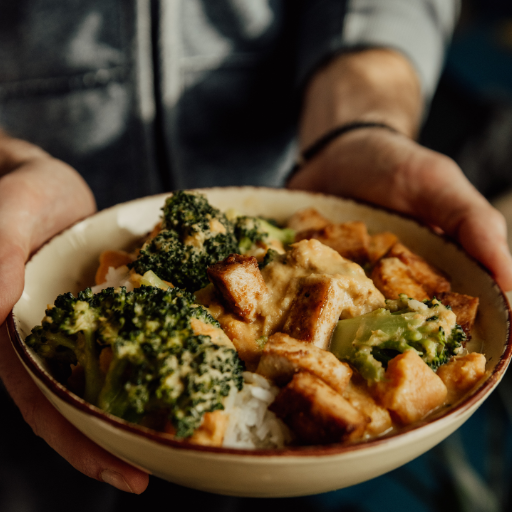 Person holding a bowl of food with broccoli and chicken.