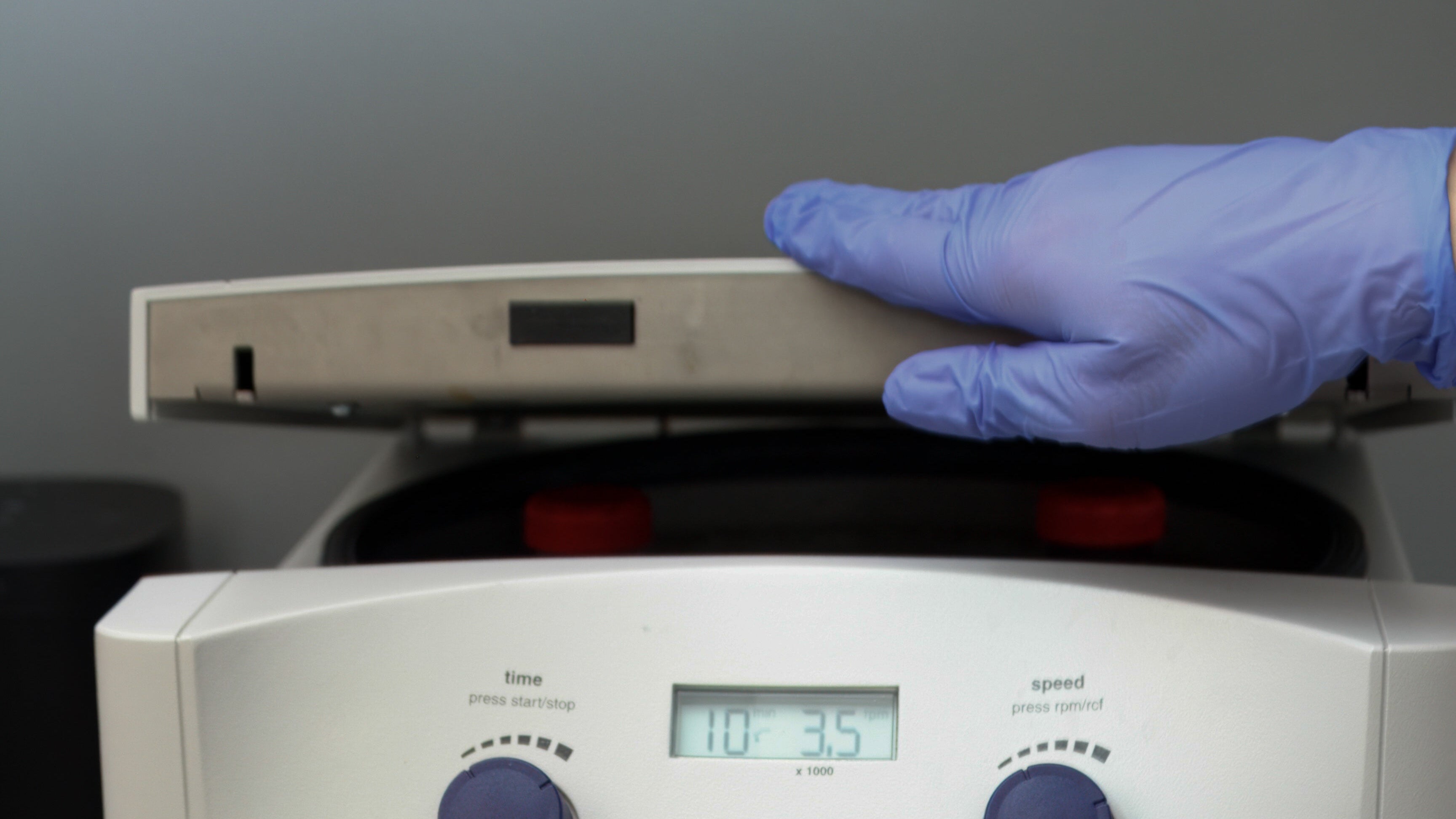 Person wearing gloves operating a laboratory centrifuge with a visible brand logo.